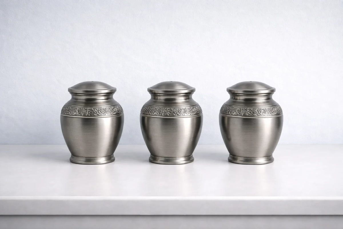 three metal keepsake urns on a counter against a light blue wall