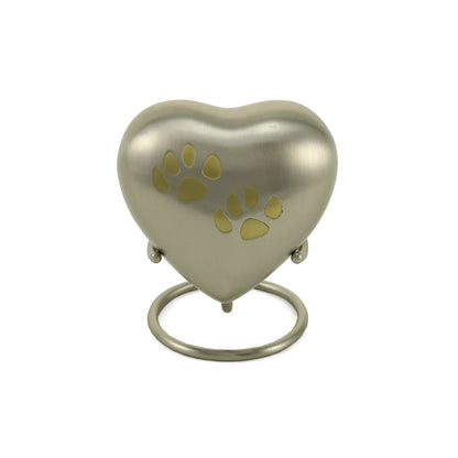 Brushed silver heart-shaped pet cremation urn featuring two gold paw print engravings, displayed on a matching circular stand