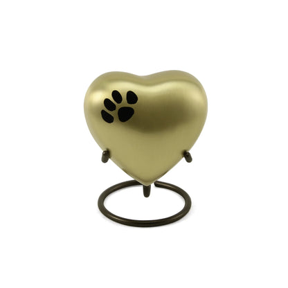 A heart-shaped pet urn with a gold metallic finish and black paw print design resting on a dark bronze ring stand on a white background