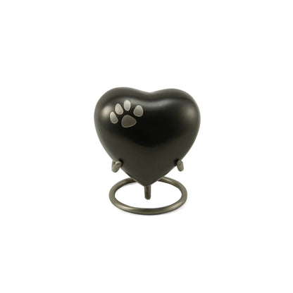 A dark grey heart-shaped pet urn with a silver paw print on its front, displayed on a metallic circular stand